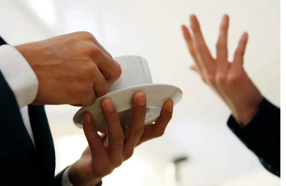 Nahaufnahme im Coaching: eine Hand reicht eine Tasse Kaffee, die andere unterstreicht ein Argument