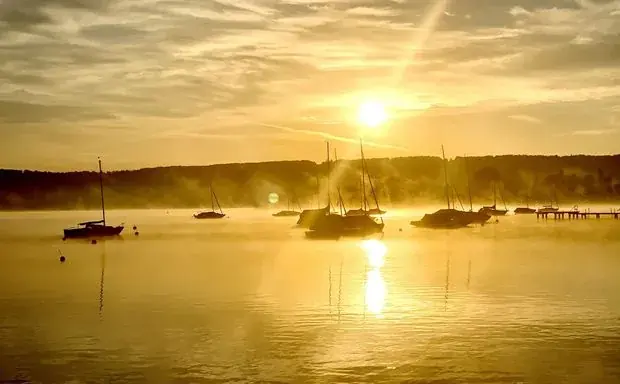 Sonnenaufgang über dem Ammersee mit vertäuten Segelbooten im Morgennebel